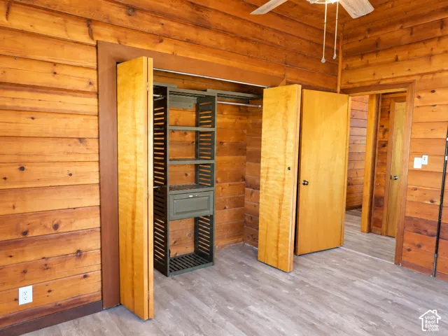 Horizontal wood-paneled walls, wood-finish flooring, built-in closet organization system, and ceiling-mounted fan