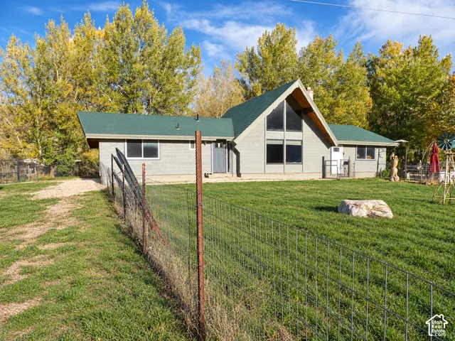 A-frame architectural structure featuring a green shingle roof, expansive floor-to-ceiling triangular windows, grey siding, and a fenced-in grassy yard