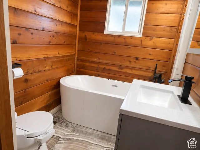 Wood-paneled walls, freestanding soaking tub, single-basin vanity with a composite countertop, and matte black plumbing fixtures