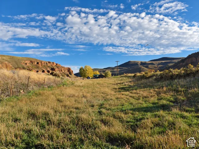 Expansive lot featuring native grassland, perimeter wire fencing, and prominent rock formations with a mountainous backdrop