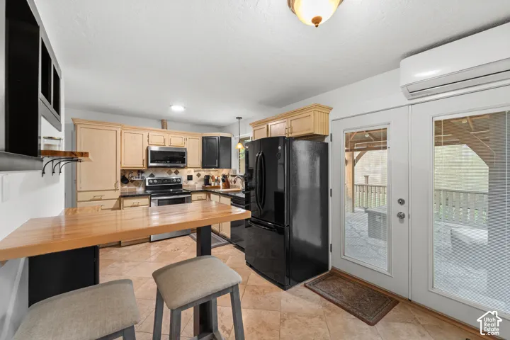 Kitchen featuring natural wood-finish cabinetry, a raised wood breakfast bar, stainless steel appliances, tile flooring, French patio door, and wall-mounted ductless climate control