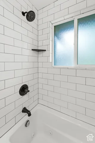 Subway tile shower surround with matte black plumbing fixtures, built-in corner shelving, and an integrated jetted tub featuring a sliding privacy window