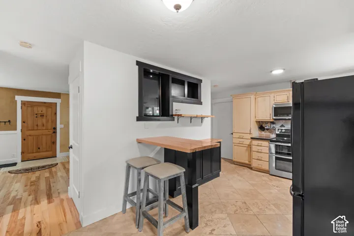 Kitchen featuring light-finish cabinetry, stone tile flooring, a black-painted breakfast bar with a wood countertop, and built-in microwave