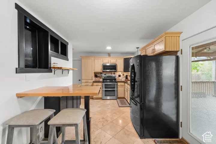Kitchen featuring stone tile flooring, a built-in breakfast bar with a natural wood-finish countertop, dual-tone cabinetry, stainless steel appliances, and a glass-paneled door