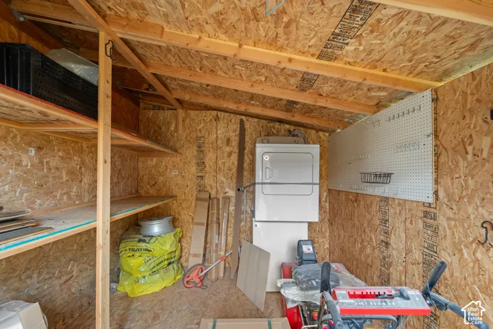 Utility shed featuring oriented strand board interior walls, built-in wooden shelving, a wall-mounted pegboard organizer, and an installed laundry appliance