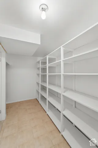 Storage space featuring floor-to-ceiling built-in white shelving, neutral tile flooring, and a flush-mount ceiling light fixture