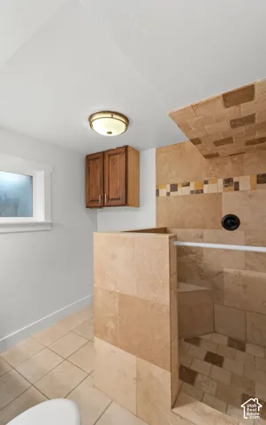 Walk-in shower featuring natural stone tiling, an integrated bench seat, decorative tile inlay, and matte black fixtures, complemented by wood-finish wall cabinetry