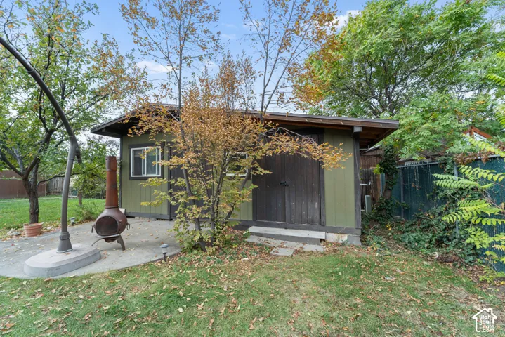Exterior structure featuring a shed with double doors, concrete patio, and mature trees within a fenced perimeter