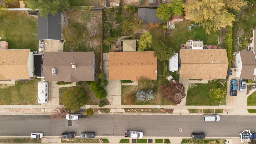 Aerial perspective of residential property featuring a concrete driveway, multi-gabled roofline, and landscaped front yard with mature trees