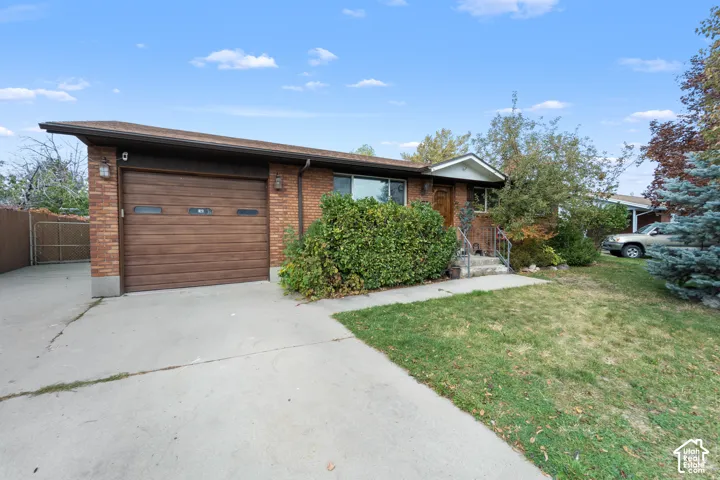 Single-story brick exterior featuring a shed-style roofline, attached single-car garage with horizontal wood-panel door, concrete driveway, and iron handrails