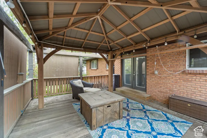 Covered wood deck featuring a timber-frame gazebo, exposed brick exterior wall, and French-style patio doors