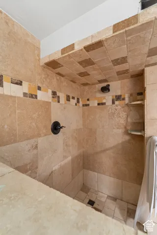 Walk-in shower featuring floor-to-ceiling stone tile, a decorative multi-colored tile inlay, built-in shelving, and dark-finish hardware