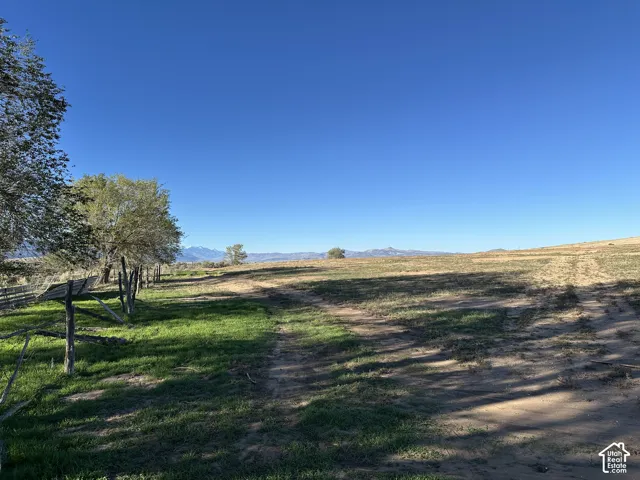 Expansive parcel of open land featuring mountain scenery, mature trees, and rustic wooden perimeter fencing