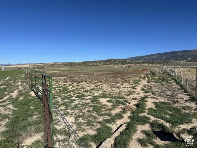 Expansive parcel of land featuring mountain backdrops, open terrain, and perimeter wire fencing with a metal gate