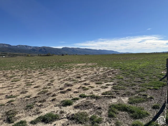 Expansive open acreage featuring native grasses, perimeter wire fencing, and prominent mountain range scenery