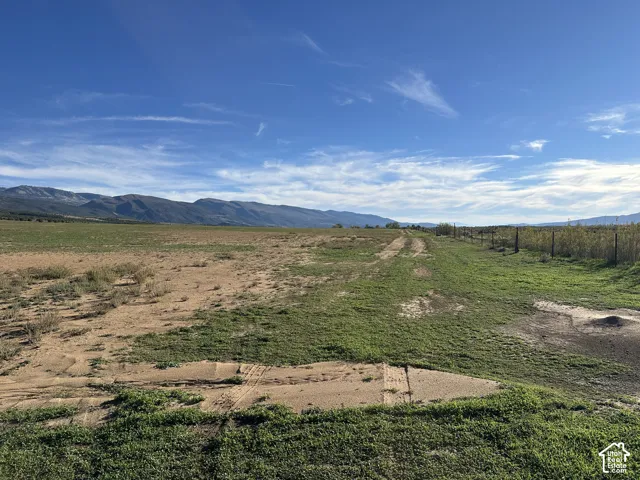 Expansive land parcel featuring native vegetation, perimeter wire fencing, and prominent mountain range scenery