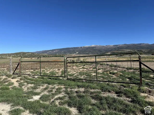 Expansive acreage featuring a metal tubular gate, wire perimeter fencing, and a mountain backdrop