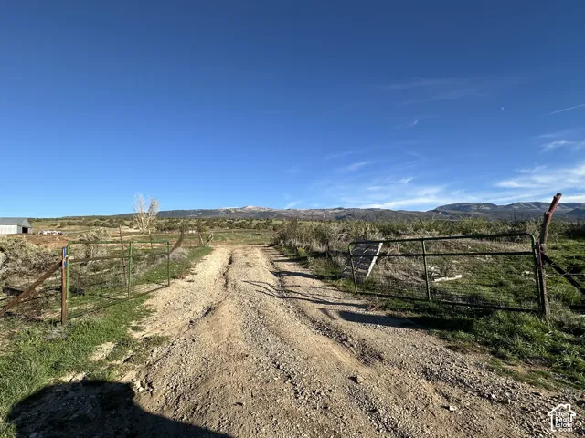 Expansive acreage featuring a gravel road, metal perimeter fencing, and mountain scenery