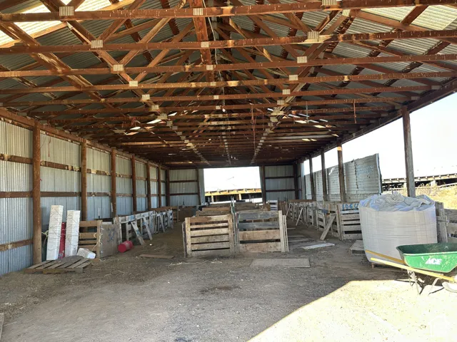 Open-span structure featuring exposed wood roof trusses, corrugated metal wall cladding, a metal roof, and compartmentalized wooden stall enclosures