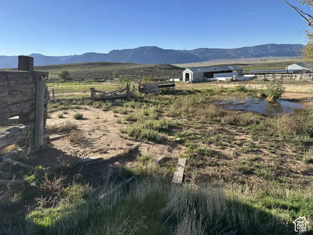 Expansive acreage featuring natural water elements, wood fencing, a metal-roof outbuilding, and mountain range scenery