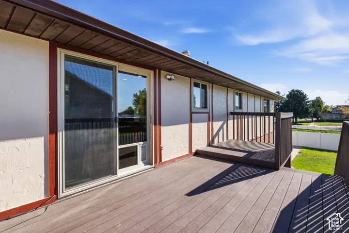 Elevated wood-tone deck featuring dark-finish balustrades, stucco exterior siding, sliding glass door, and attached wall-mounted lighting