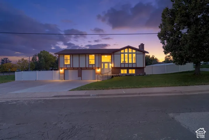 Split-level exterior featuring a combination of brick and panel siding, large multi-pane windows, a two-car garage, and a vinyl privacy fence
