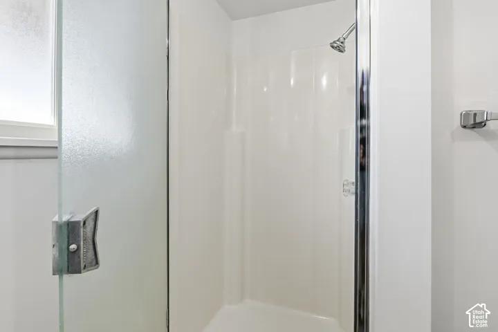 Shower enclosure featuring a molded surround, semi-frameless glass door with metal hardware, wall-mounted shower head, and chrome-finish towel bar