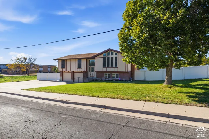 Split-level exterior featuring a brick and timber-frame facade, large-paned front windows, a two-car garage, and an enclosed vinyl fence