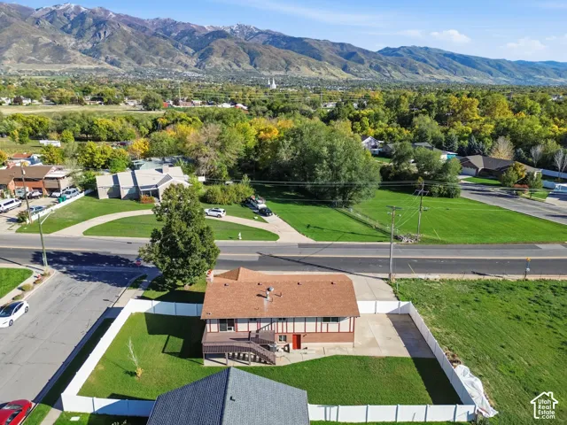 Aerial perspective featuring a multi-level residence with brick and wood siding, an elevated rear deck, a fully fenced backyard with lawn, and a mountain range backdrop