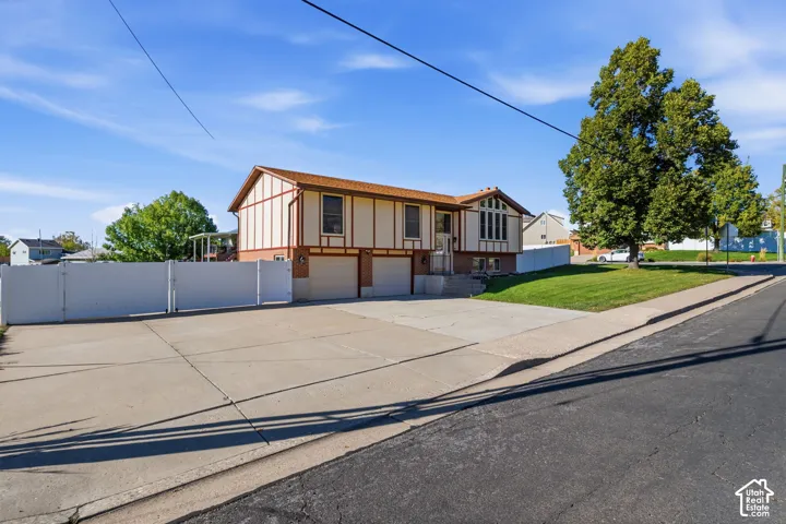 Two-story exterior featuring timber-frame detailing, an attached two-car garage, concrete driveway, and white vinyl perimeter fencing