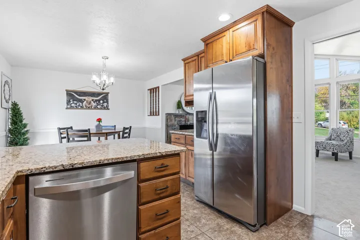 Kitchen featuring natural wood cabinetry, stone-patterned countertops, stainless steel appliances, tile flooring, and a multi-light chandelier