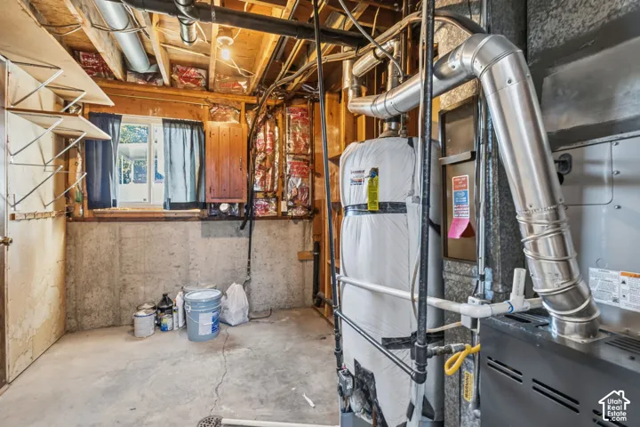 Utility area featuring a concrete foundation wall, exposed wood-joist ceiling, thermal insulation, water heater, and furnace system with metal ductwork