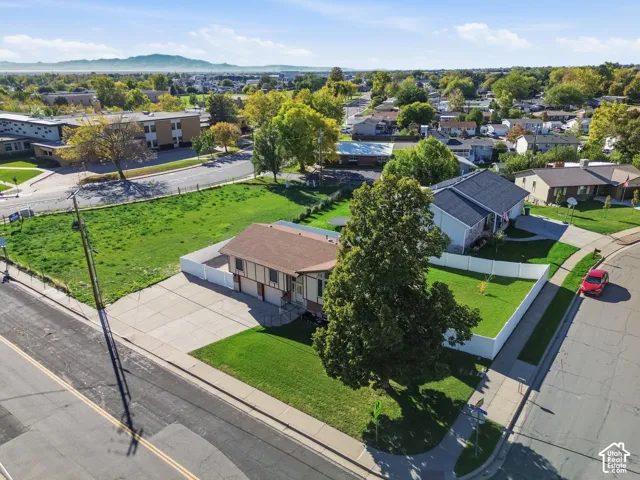 Corner lot featuring a multi-level residence with a side-loading garage, concrete driveway, white vinyl fencing, and mature trees