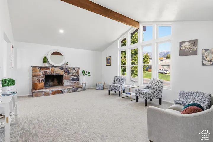 Vaulted ceilings with exposed wooden beam, floor-to-ceiling stone fireplace, and oversized picture windows