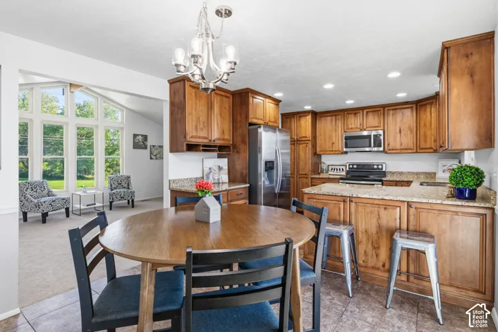 Kitchen featuring wood cabinetry, stone countertops, stainless steel appliances, tile flooring, and a multi-arm chandelier