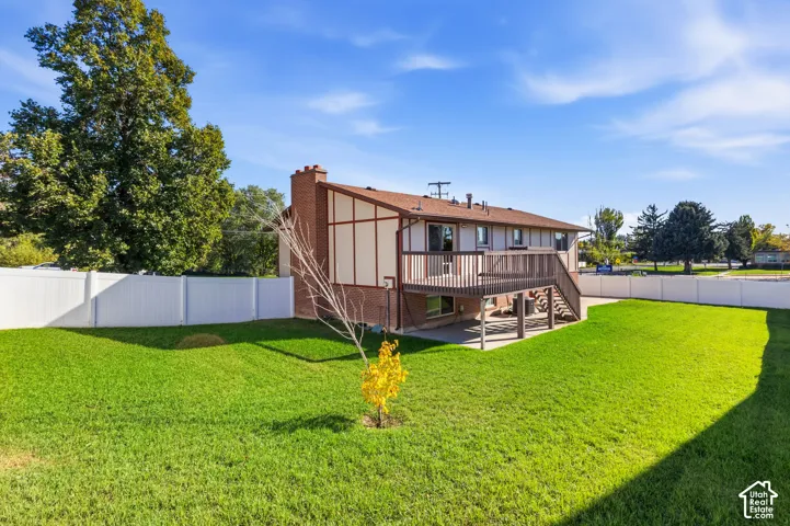 Expansive backyard featuring a manicured lawn, full-perimeter white vinyl fencing, a raised wood deck, and a brick chimney exterior