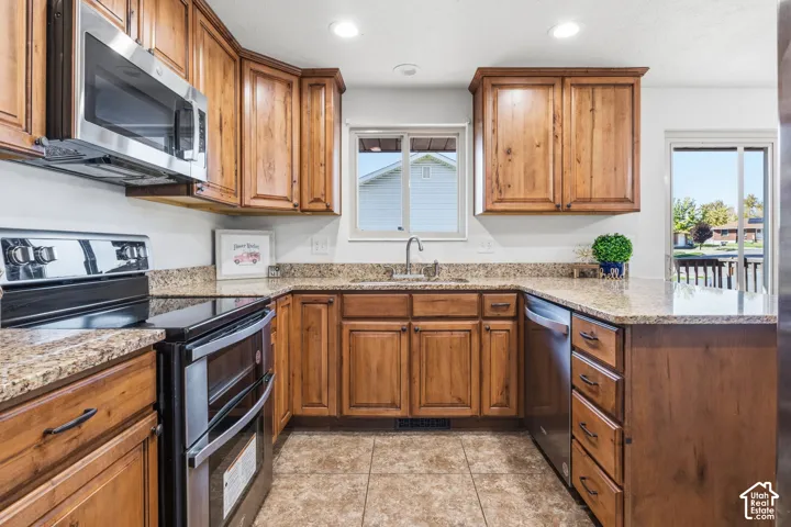 Kitchen featuring stained wood cabinetry, stone-finish countertops, stainless steel appliances, tile flooring, and a double-basin sink