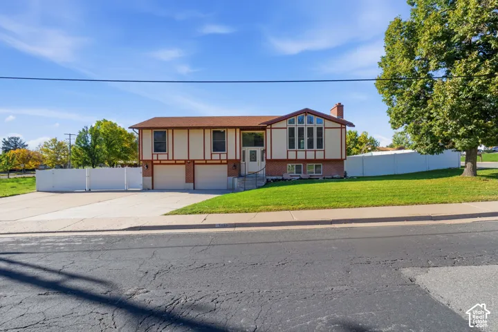 Split-level exterior featuring brick and wood-trim siding, a two-car garage, multi-pane bay windows, and a privacy fence