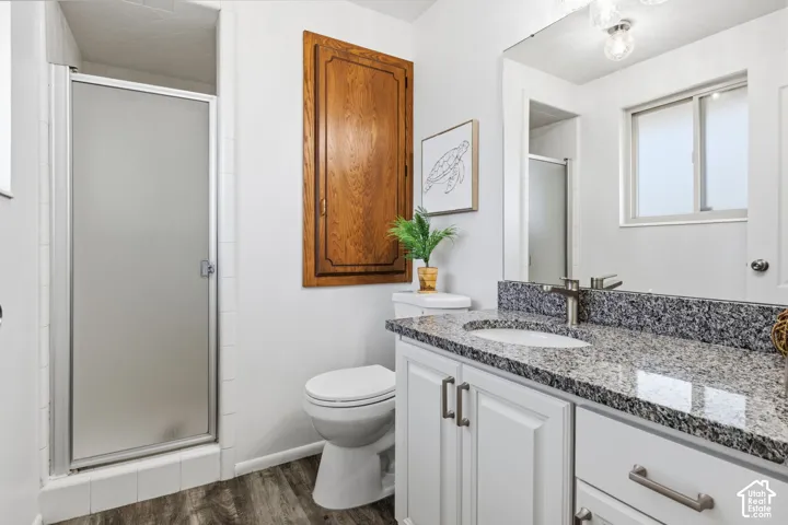 Bathroom featuring white cabinetry, stone-surface countertop, integrated oval sink, walk-in shower with frosted glass door, and wood-finish flooring