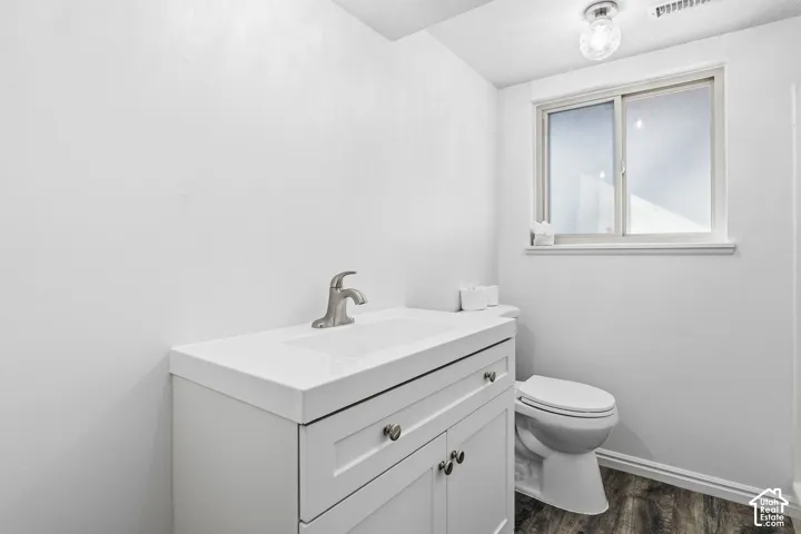 White shaker-style vanity with a solid countertop, integrated basin, brushed nickel faucet, and wood-finish flooring