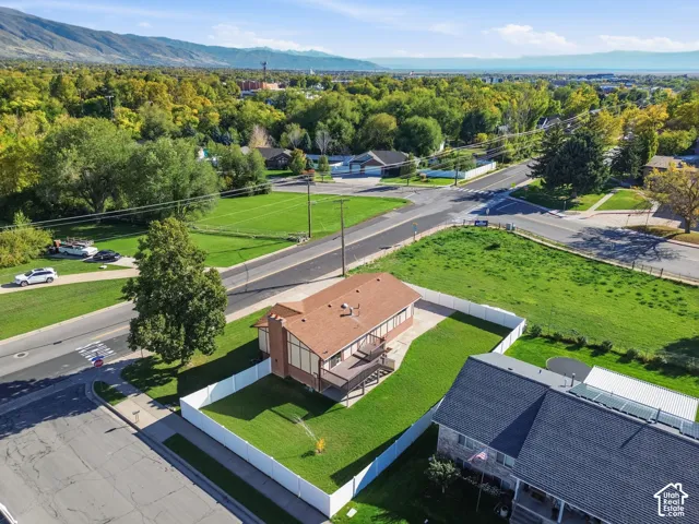 Aerial perspective of a detached residence featuring a wood-frame deck, fenced yard, brick chimney, and mountainous backdrop