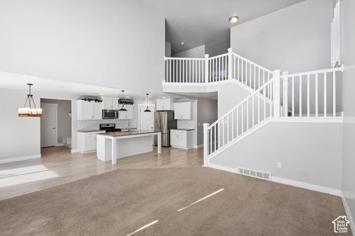 High-ceiling interior featuring a central staircase with white balusters, kitchen with white cabinetry and a center island, and wood-finish flooring