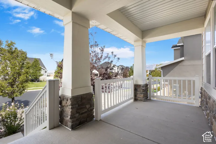 Covered porch featuring concrete flooring, stone-veneer column bases, white railings, and substantial architectural columns