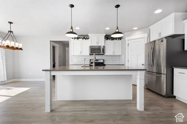 Kitchen featuring white cabinetry, a center island with a stone-surface countertop, a herringbone-pattern tile backsplash, stainless steel appliances, and wood-finish flooring
