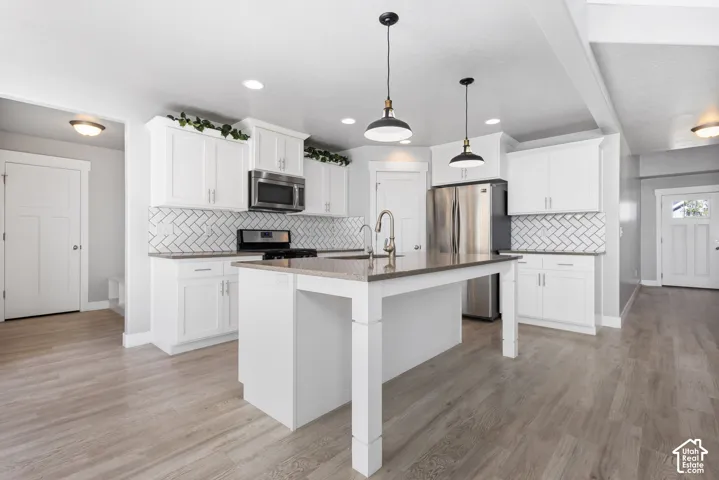Kitchen featuring white shaker-style cabinetry, central island with stone-finish countertop, stainless steel appliances, herringbone-pattern tile backsplash, and wood-finish flooring