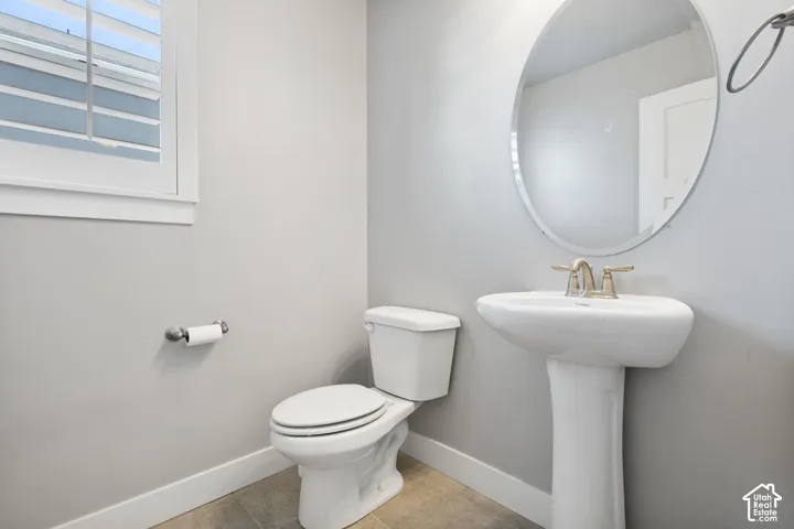 Pedestal sink with metallic faucet, oval wall-mounted mirror, white toilet, and window with shutter blinds