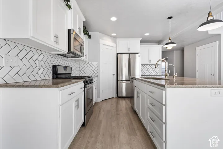 Kitchen featuring white cabinetry, stone-finish countertops, stainless steel appliances, herringbone-pattern tile backsplash, and wood-finish flooring