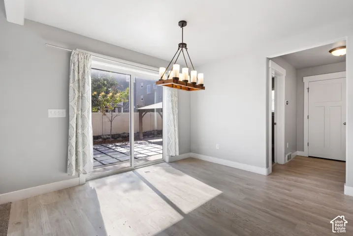 Wood-finish flooring, linear wood-beam chandelier with cylindrical glass shades, sliding glass patio door, and three-panel interior door
