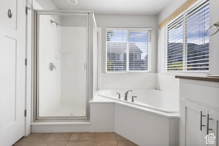 Bathroom featuring a corner soaking tub, separate glass-enclosed shower, tile flooring, and white cabinetry with metal hardware