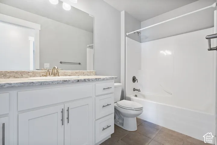 Bathroom featuring white cabinetry, stone-finish countertop with an integrated basin, large vanity mirror, tile flooring, and a shower-tub combination